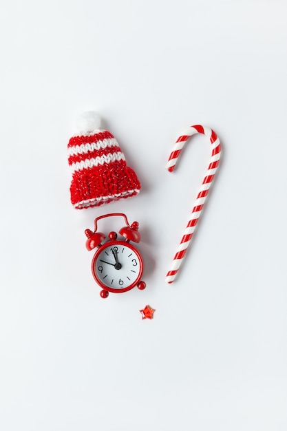 Christmas composition, cane candy, small analog clock, striped hat, star, laid out in shape of heart on white background.media, greeting card.