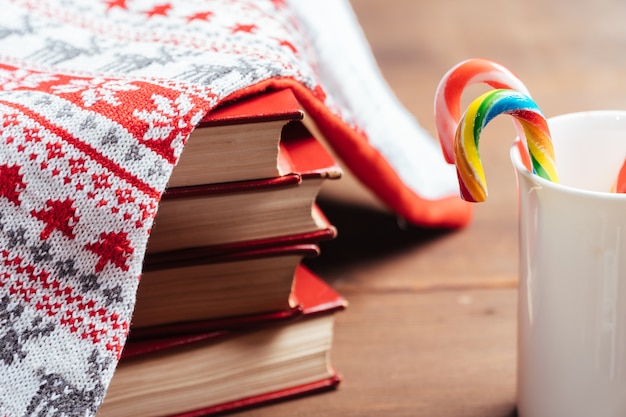 Christmas composition: colored candy canes in a cup with books on wooden desktop