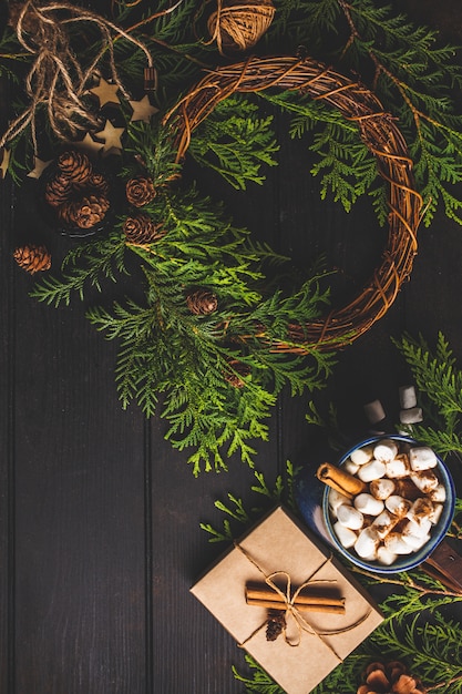 Рождественская композиция на темном фоне. Рождественский венок, какао, подарочная коробка и рождественские украшения фона.