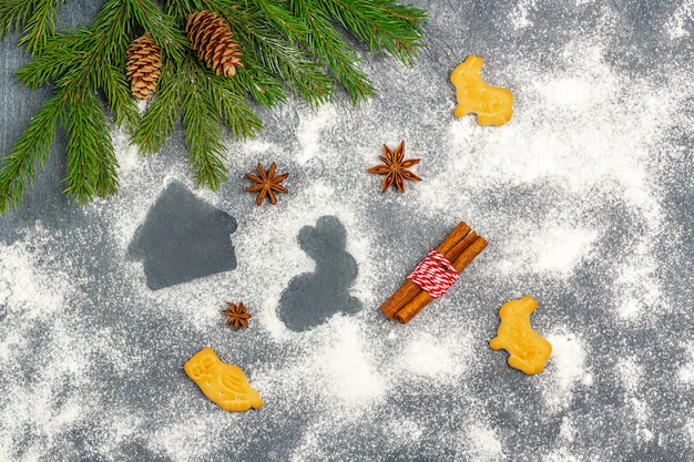 Composizione di natale. farina silhouette di biscotti su sfondo scuro tra i rami degli alberi di natale, coni, anice stellato e cannella.