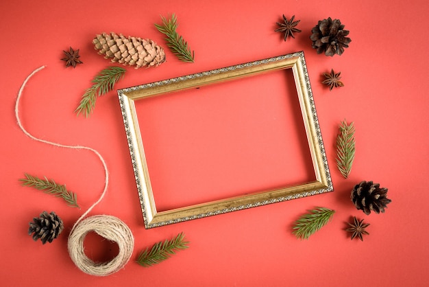 Foto composizione in natale di confezione regalo, rami di abete, coni, fiocco rosso su fondo rosso.