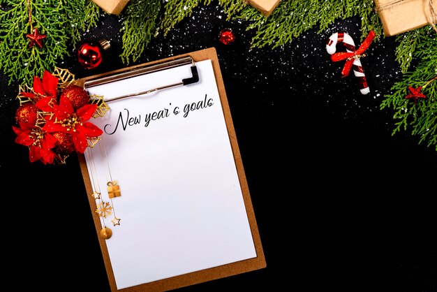 Christmas composition. Girlanda with Christmas ornaments and gifts on black background and blank notepad