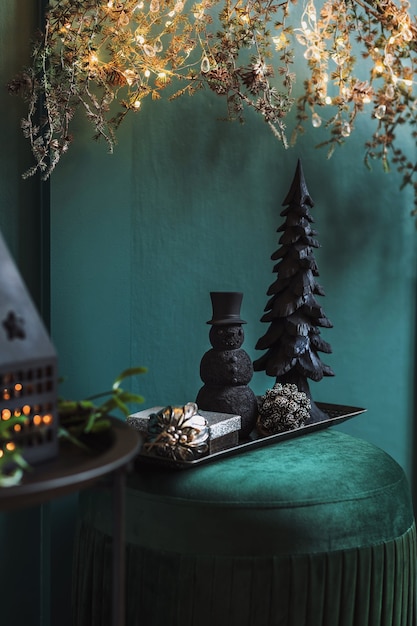 Christmas composition on the green velvet pouf in living room. Beautiful decoration. Christmas trees, candles, stars, lights and elegant accessories. Merry Christmas and Happy Holidays, Template.