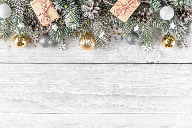 Christmas composition made of snowy fir tree, gift boxes and\
decorations on white wood background. flat lay