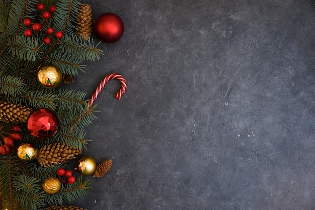 Рождественская композиция из еловых веток, елочные шары, конфеты и шишка на темном