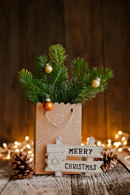 Christmas composition. Paper bag with and bumps fir branches on brown wooden  and bokeh lights.