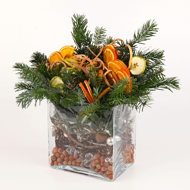 Christmas composition of pine branches, apple and orange
slices, pine cones, bark and hazelnuts. in plain glass rectangular
vase. on white background