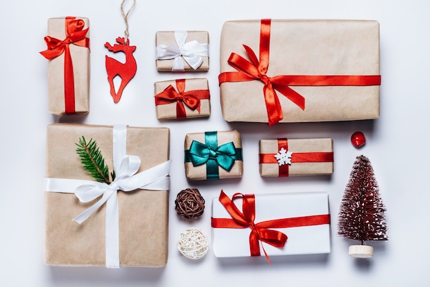 Photo christmas composition of various gift boxes wrapped in craft and white paper and decorated with satin red ribbons. top view, flat lay.