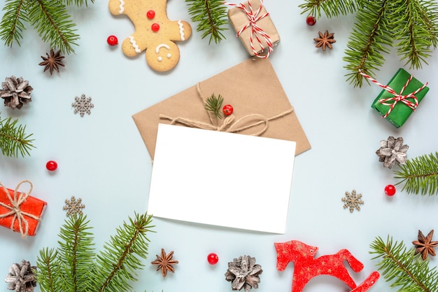 Фото Рождественская композиция с пустой поздравительной открыткой в рамке из еловых веток, украшений и подарочных коробок на синем фоне. макет. плоская планировка. вид сверху
