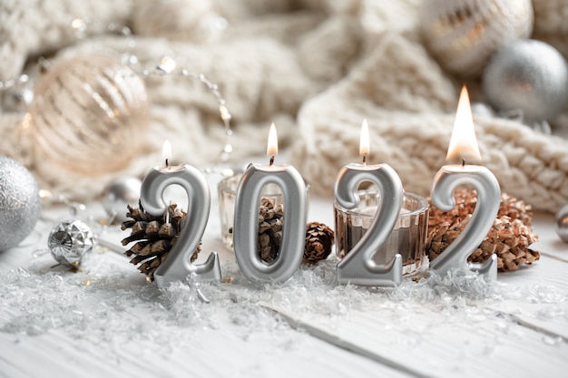 Composizione natalizia con candele a forma di numeri 2022 e dettagli decorativi festivi su uno sfondo sfocato.