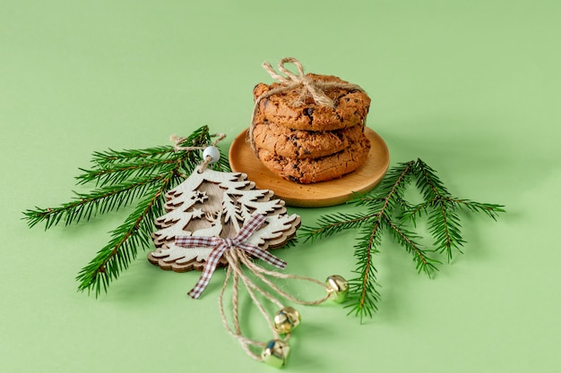 モミの木の枝と木のおもちゃと緑の紙にチョコレートチップクッキーとクリスマスの構成。お祝いのグリーティングカード。