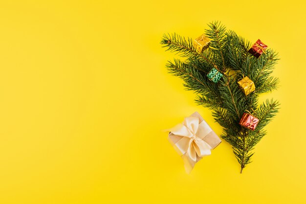 Christmas composition with Conifer Evergreen tree branches and gift box on yellow
