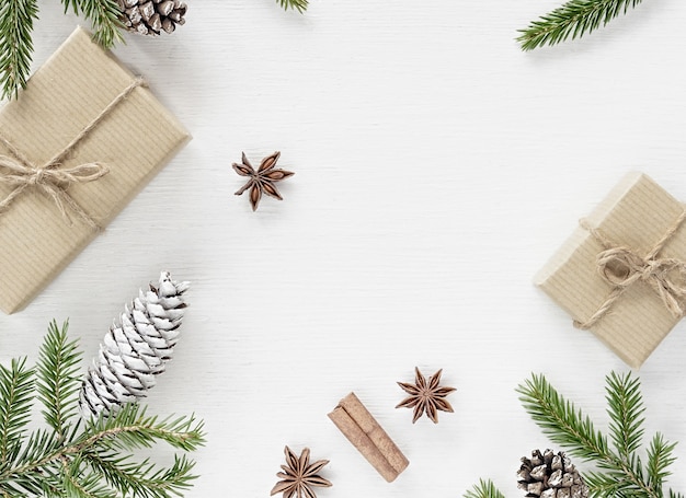 Christmas Composition with gift boxes wrapped in kraft paper, fir branches pine cones and christmas spices on white wooden background. Copy space, flat lay