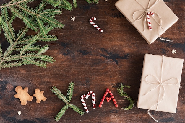 Composizione in natale con regalo e omino di pan di zenzero su fondo scuro di legno. testo di natale di natale, pigne, rami di abete sulla scrivania di legno, vista piatta e dall'alto, spazio per le copie