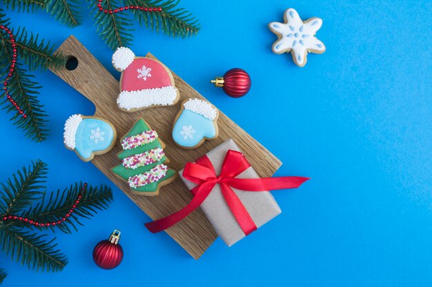 Christmas composition with gingerbread and gift box on the wooden cutting board  on the blue background. Top view. Copy space.