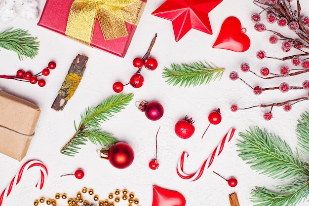 Christmas composition with golden garland red gift green Xmas fir branch red holly berries and baubles on white stucco plaster texture background Top view flat lay