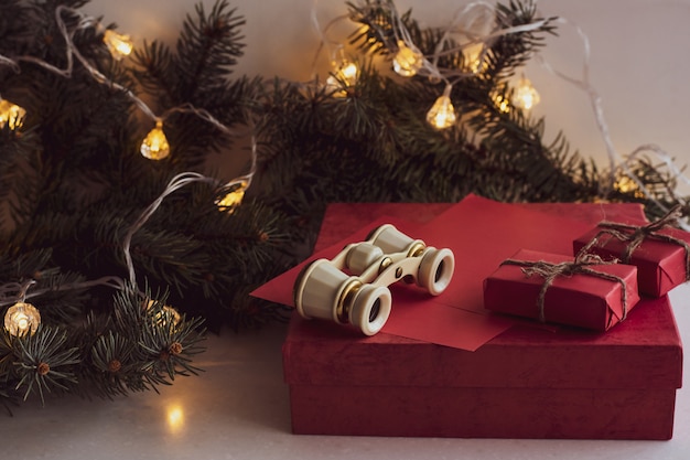 Christmas composition with opera glasses, fir branch, red gift boxes and garland