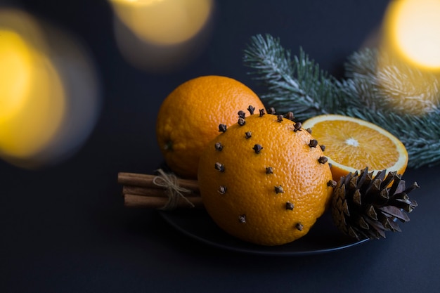 Christmas composition with oranges, spice cloves and cinnamon on the black plate on the black  background. Close-up.