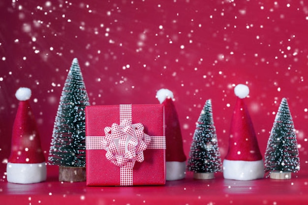 Composizione natalizia con scatola regalo rossa e albero di natale e cappelli di babbo natale su sfondo rosso concetto di vacanza