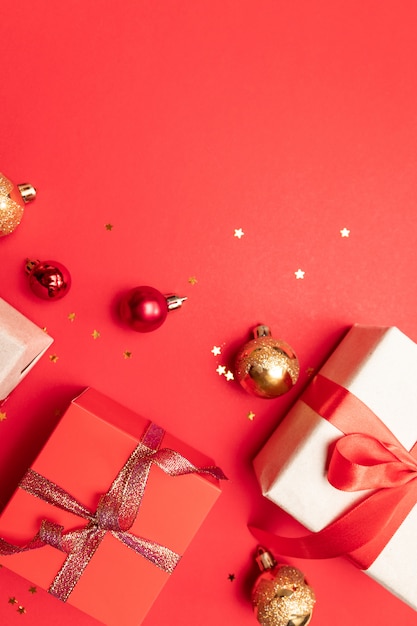 Christmas composition with red present box, ribbons, red gold big and small balls, holiday decorations on red . Flat lay, top view, copyspace