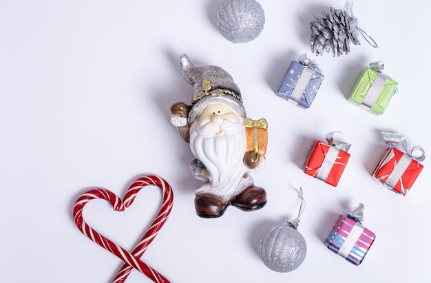 Christmas composition with Santa Claus or gnome, gifts, Christmas candy canes in the shape of a heart, purple and silver balls, pine cones on a white background, Flat lay, top view, copy space