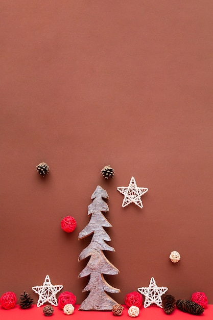 Новогодняя композиция с деревянной елкой, сосновыми шишками, звездами на красном столе