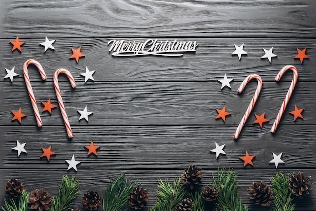 Christmas composition: wooden grey background with fir tree, pine cones, Christmas cane, red and white stars