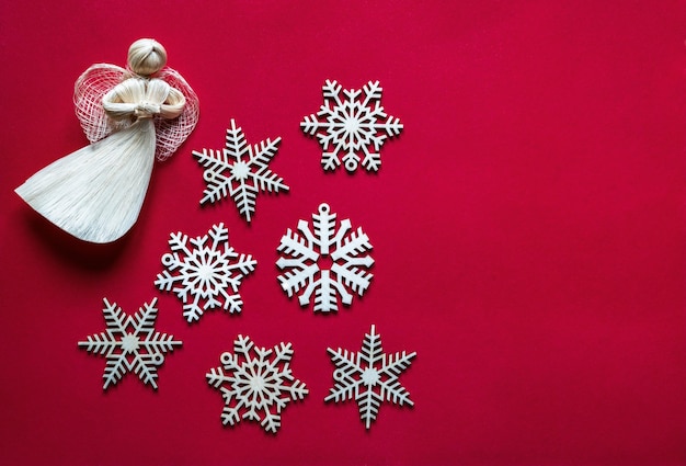 Foto composizione natalizia. fiocchi di neve in legno e angelo di paglia su uno sfondo di tessuto rosso