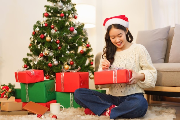 Christmas concept Asian woman sitting in christmas decorated living room and open christmas gift