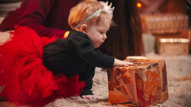 Photo christmas concept a cute little baby with a bow on the rim playing with a gift box