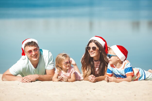 クリスマスのコンセプト。ビーチでクリスマスの帽子をかぶっている家族