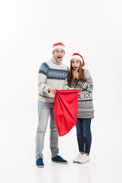 Christmas Concept - Full length Jonge aantrekkelijke paar bedrijf santa tas geïsoleerd op wit grijze muur.