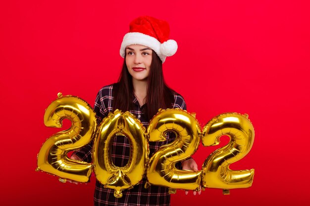 Christmas , concept of a happy holiday - a young woman in pajamas and a Santa Claus hat holds the numbers 2022