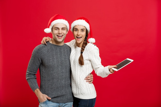 Christmas concept - Happy young couple in christmas sweaters holding digital tablet.