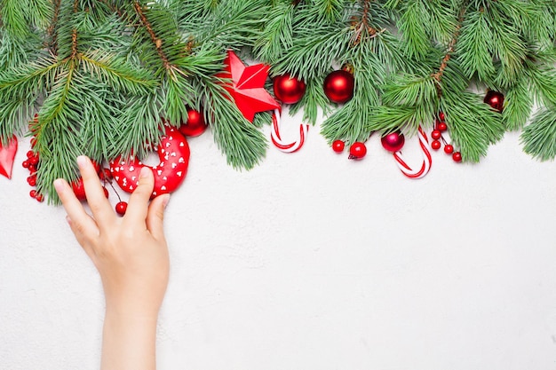 Christmas concept Little baby girl hand with donut green Xmas fir branch red holly berries and baubles on white background Colorful Christmas composition top view flat lay with copy space