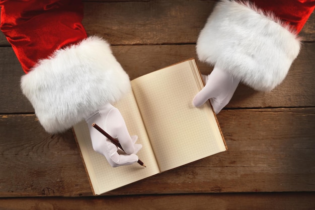 Christmas concept. Santa Claus hands  write in notebook on wooden background