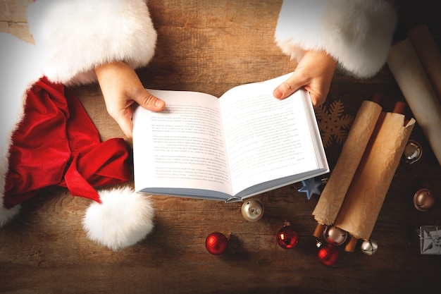 Фото Рождественское понятие. санта руки с книгой и рождественскими украшениями на деревянном столе, крупным планом
