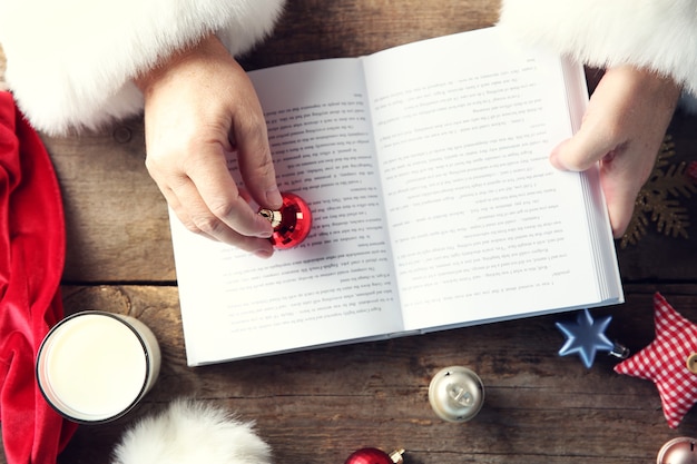 Concetto di natale. mani di babbo natale con libro e decorazioni natalizie sul tavolo di legno, primo piano