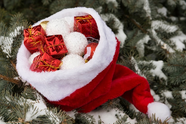 Foto concetto di natale, su un abete naturale innevato, il cappello di babbo natale è pieno di decorazioni di regali