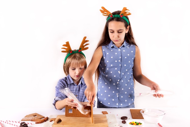クリスマスのコンセプト2人の子供が白い背景で隔離のジンジャーブレッドの家を作るクリスマスカード