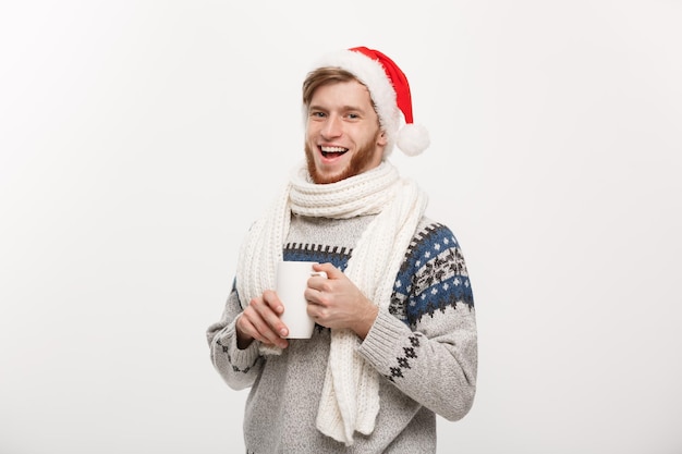 Christmas concept Young beard man in sweater and santa hat holding a hot coffee cup isolated on white with copy space