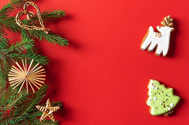 Christmas cookies and decorated fir tree branches on red background