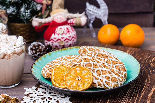 Christmas cookies and dried mandarin slices in a plate and hot cocoa with marshmallows in glasses on table with Christmas decorations