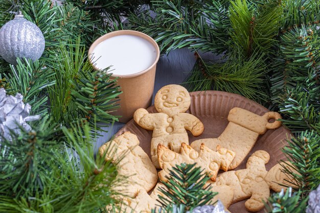 Christmas cookies, gingerbread cookies and a glass of milk in a craft glass for Santa with fir branches and Christmas decorations. Christmas background.