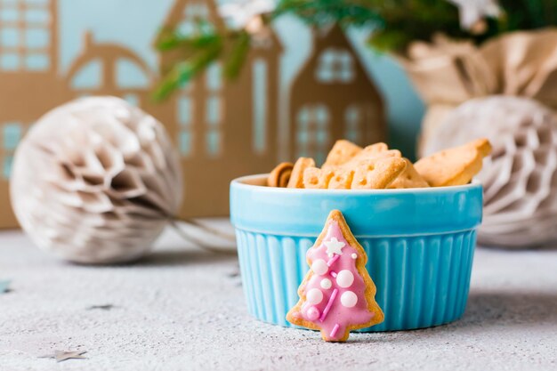 Christmas cookies spruce with pink icing are placed near a bowl of cookies on a decorated table. Festive treat