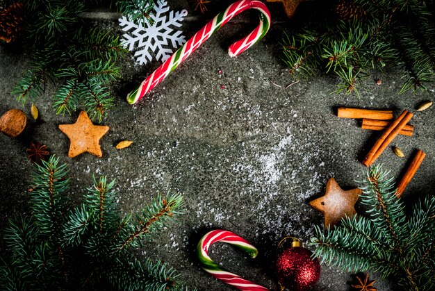 Рождественский темный фон с еловыми ветками, сосновыми шишками, конфетами, подарками, елочными шарами и украшениями