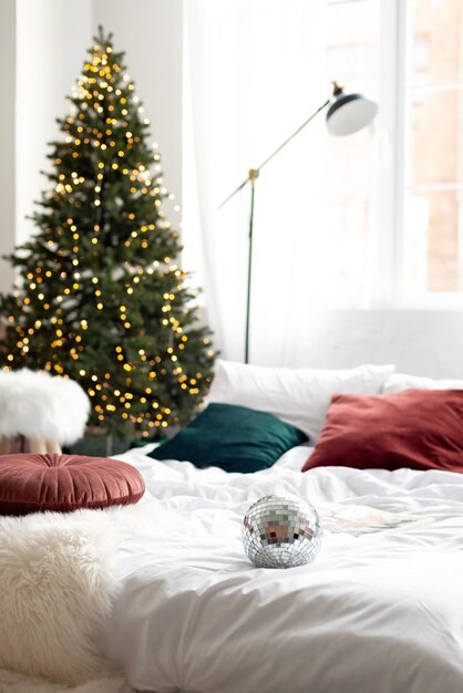 Christmas decor. bedroom in light colors with a large bed. the\
interior is decorated with garlands, christmas wreaths and a new\
year tree in a modern style. soft selective focus.