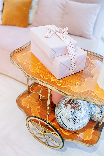Новогодний декор в светлых тонах, праздничные подарочные коробки на декоративной тележке с диско-шарами