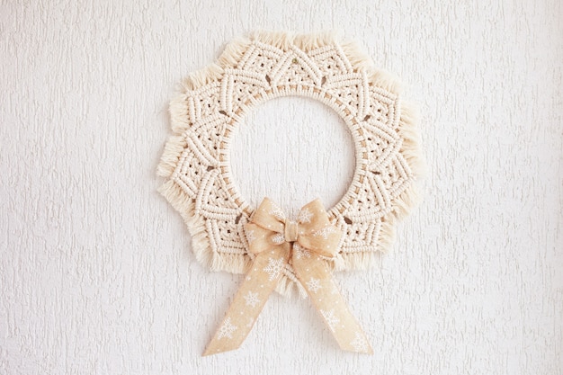 Christmas decor. Macrame wreath for Christmas and the new year on a white decorative plaster wall. Natural cotton thread, linen tape. Eco decor for home