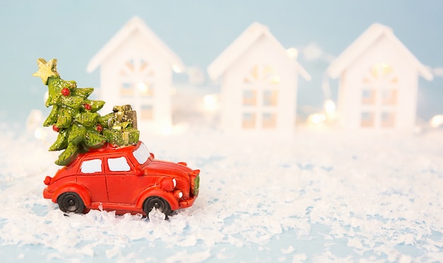 Christmas decor, red retro car on snow carries Christmas tree near houses